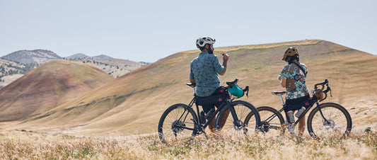 Two people sat by their bikes, looking out on a wide landscape